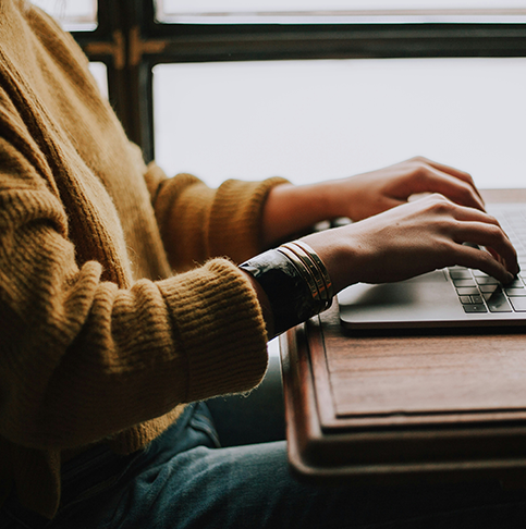 Frau mit gelbem Pullover tippt auf einer Laptoptastatur