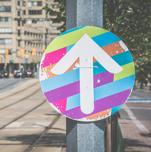 Rundes buntes Schild an einer Laterne mit einem weißen Pfeil darauf