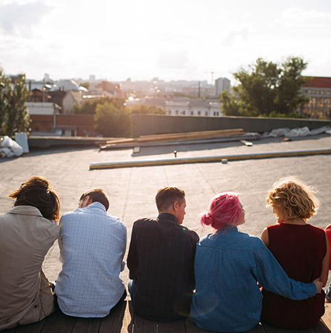 Eine Gruppe junger Menschen sitzen in einer Reihe nebeneinander auf einem Dach